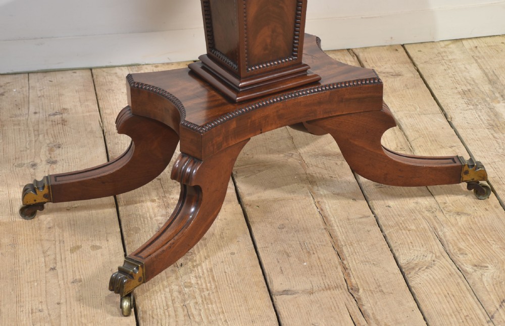 A Regency mahogany tea table featuring a fold-over top, central pedestal support, and four splayed legs with brass paw castors. View X