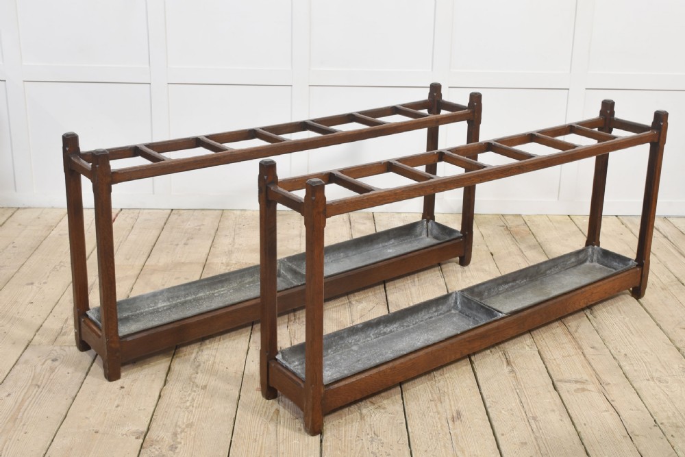 A pair of long dark oak Gothic Revival umbrella stands featuring divided top compartments and metal drip trays.