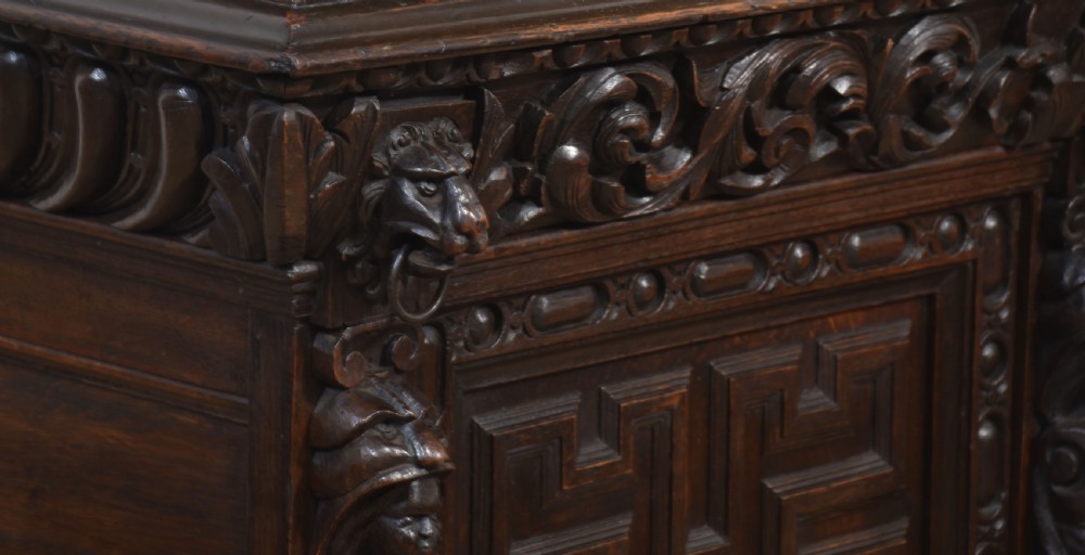 A tall dark oak Renaissance Revival bookcase featuring two glazed upper doors, intricate carved relief details, and geometric carved lower cupboard panels. View VI