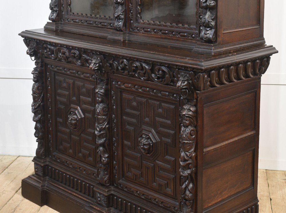 A tall dark oak Renaissance Revival bookcase featuring two glazed upper doors, intricate carved relief details, and geometric carved lower cupboard panels. View XV
