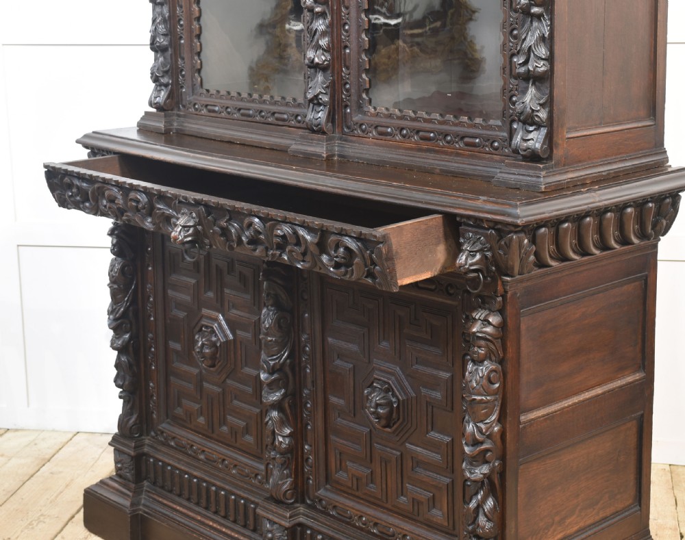 A tall dark oak Renaissance Revival bookcase featuring two glazed upper doors, intricate carved relief details, and geometric carved lower cupboard panels. View XVI