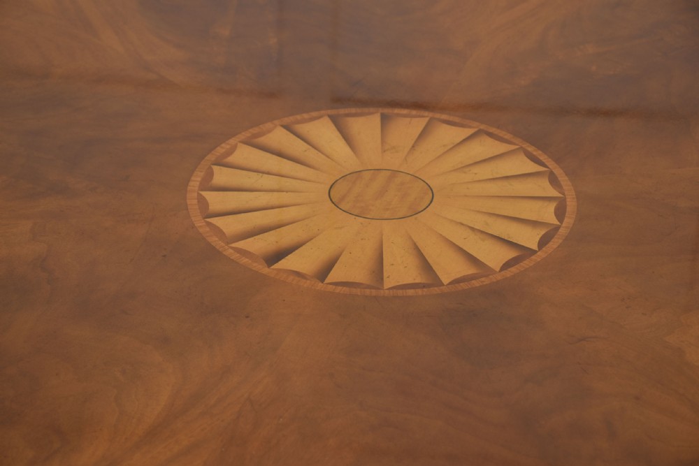 A circular mahogany dining table featuring crossbanded veneer edging, a central revolving lazy susan with marquetry inlay, and a pedestal support with four reeded legs terminating in brass castors. View III