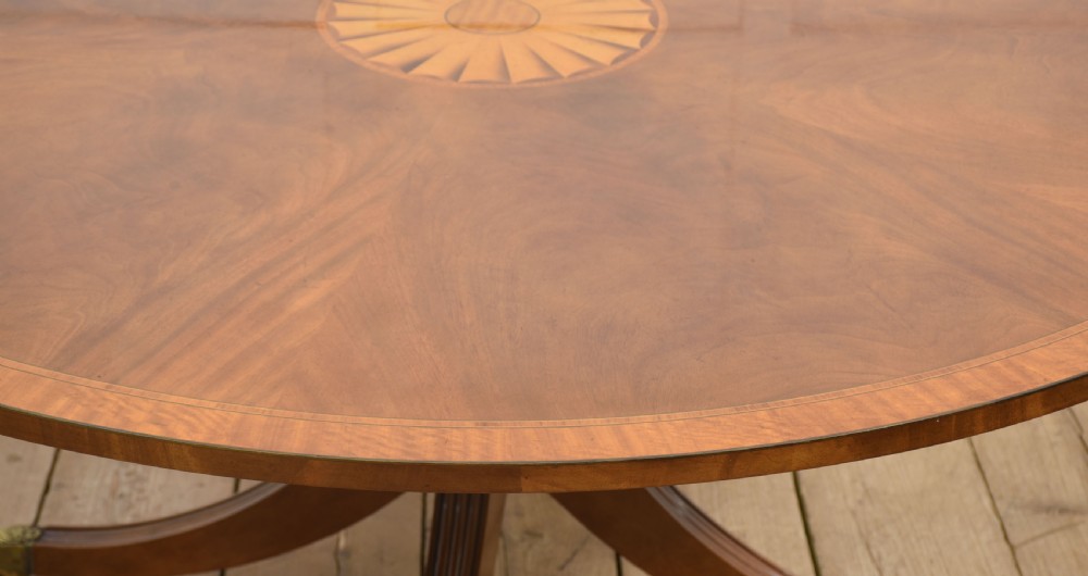 A circular mahogany dining table featuring crossbanded veneer edging, a central revolving lazy susan with marquetry inlay, and a pedestal support with four reeded legs terminating in brass castors. View VI