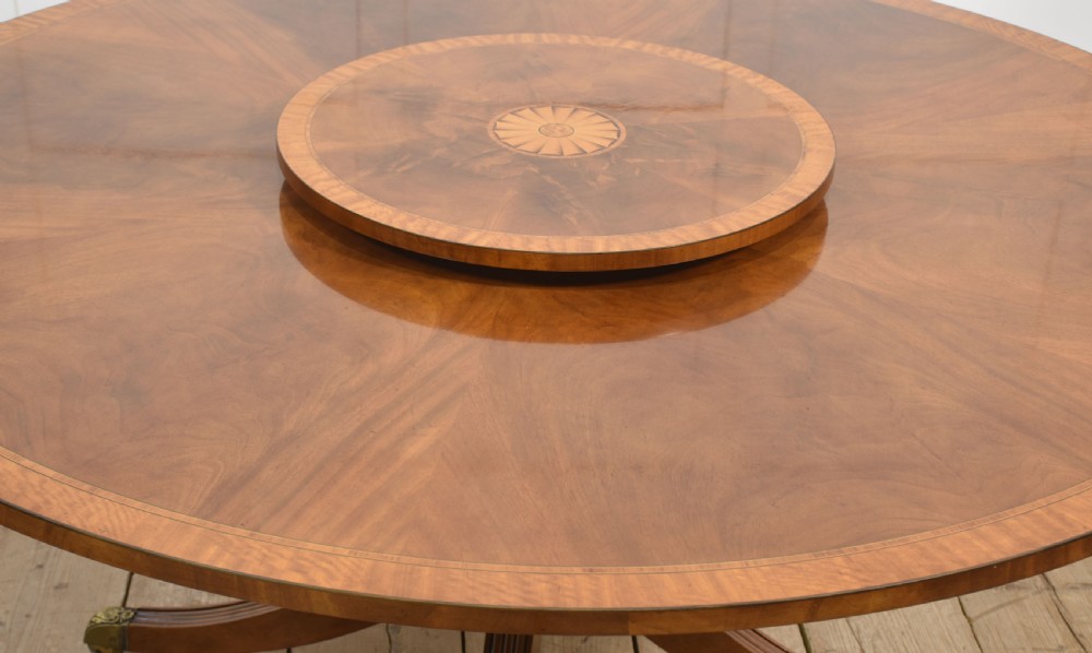 A circular mahogany dining table featuring crossbanded veneer edging, a central revolving lazy susan with marquetry inlay, and a pedestal support with four reeded legs terminating in brass castors. View VII