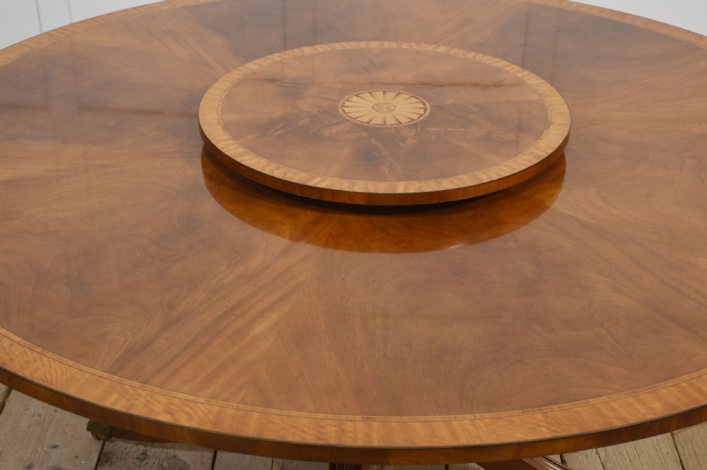 A circular mahogany dining table featuring crossbanded veneer edging, a central revolving lazy susan with marquetry inlay, and a pedestal support with four reeded legs terminating in brass castors. View VIII