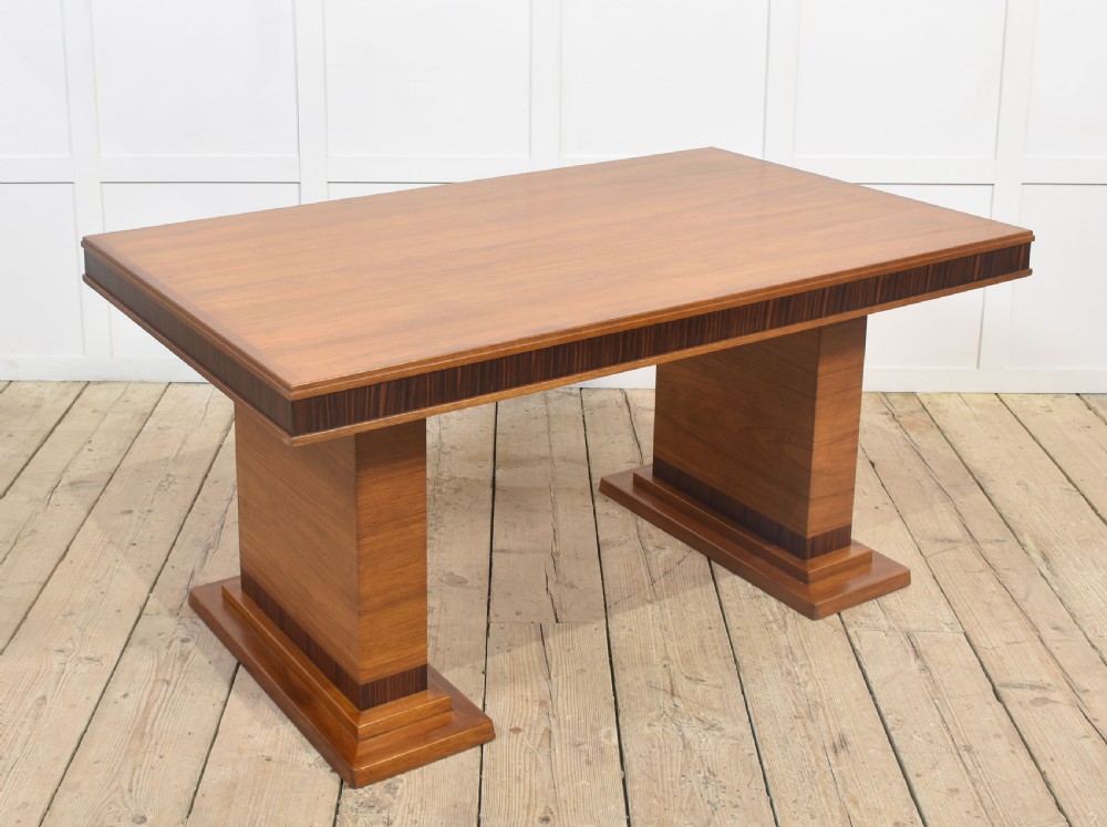 An Art Deco rectangular walnut dining table featuring twin block pedestal supports and dark crossbanded border details along the apron.