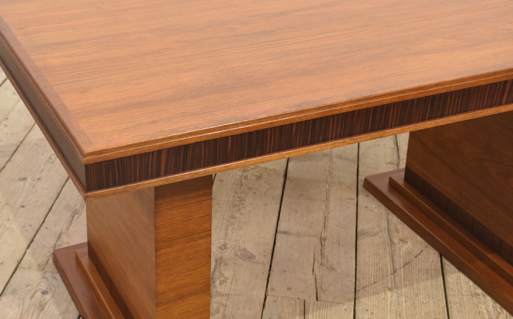 An Art Deco rectangular walnut dining table featuring twin block pedestal supports and dark crossbanded border details along the apron. View V