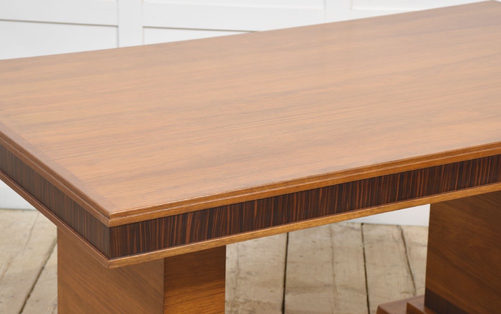 An Art Deco rectangular walnut dining table featuring twin block pedestal supports and dark crossbanded border details along the apron. View VI