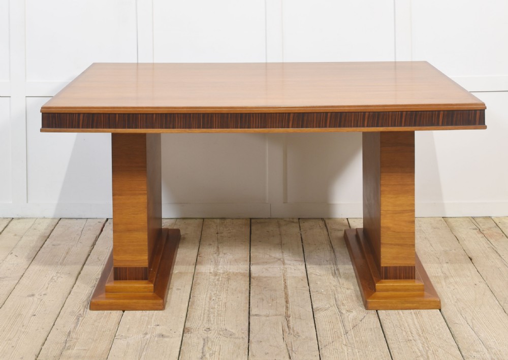 An Art Deco rectangular walnut dining table featuring twin block pedestal supports and dark crossbanded border details along the apron. View X