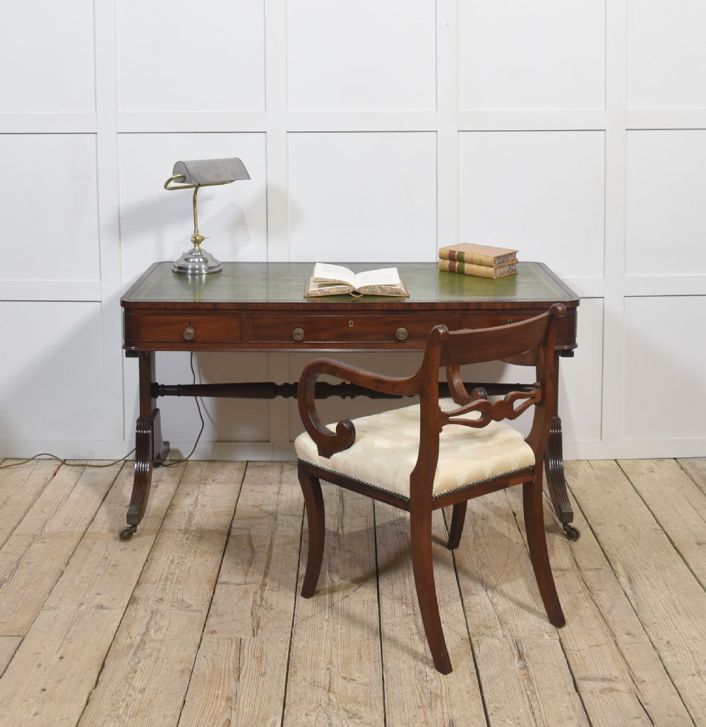 A Regency mahogany library table featuring a green leather inset top, brass knob drawers, a turned central stretcher, and reeded sabre legs on brass castors. View II