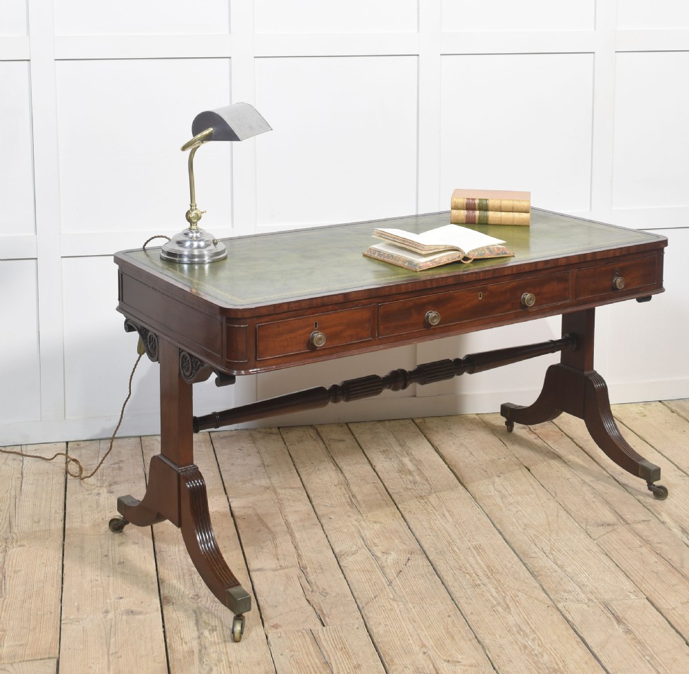 A Regency mahogany library table featuring a green leather inset top, brass knob drawers, a turned central stretcher, and reeded sabre legs on brass castors. View VI