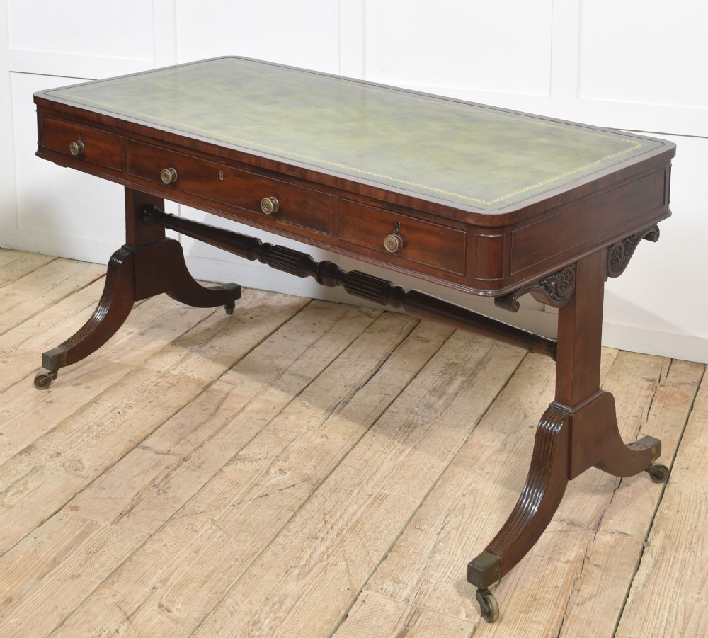 A Regency mahogany library table featuring a green leather inset top, brass knob drawers, a turned central stretcher, and reeded sabre legs on brass castors. View IX