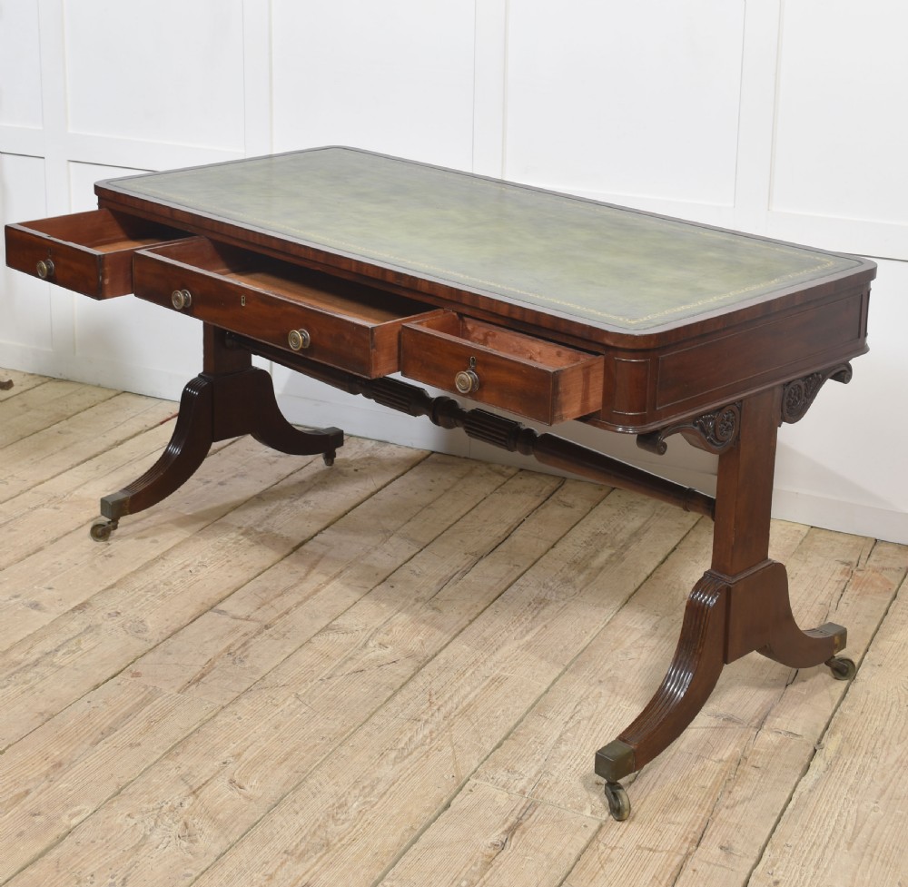A Regency mahogany library table featuring a green leather inset top, brass knob drawers, a turned central stretcher, and reeded sabre legs on brass castors. View XI