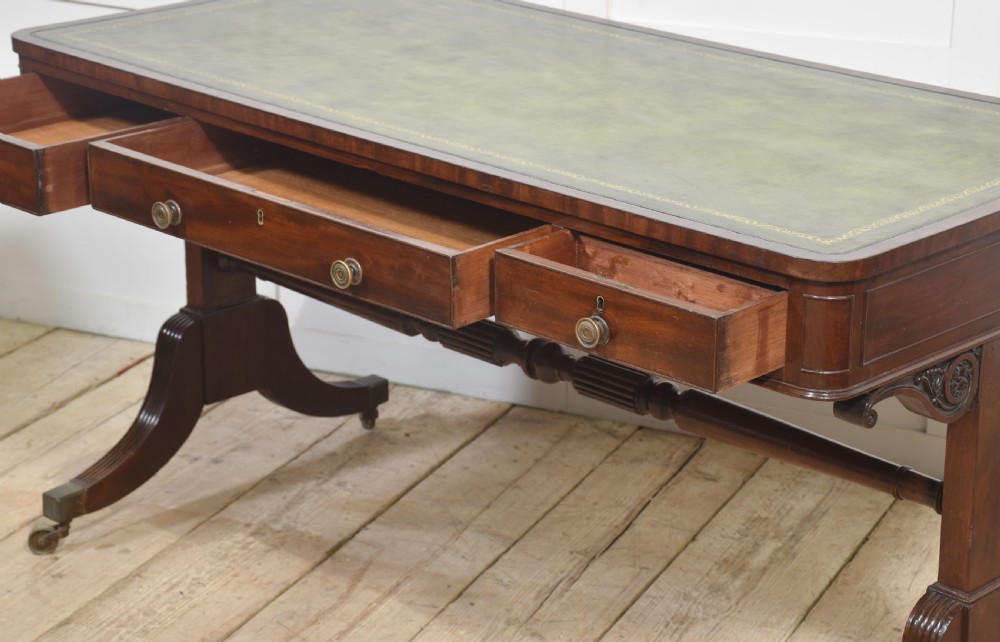 A Regency mahogany library table featuring a green leather inset top, brass knob drawers, a turned central stretcher, and reeded sabre legs on brass castors. View XII