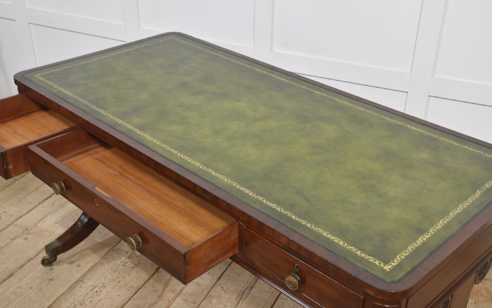 A Regency mahogany library table featuring a green leather inset top, brass knob drawers, a turned central stretcher, and reeded sabre legs on brass castors. View XIII