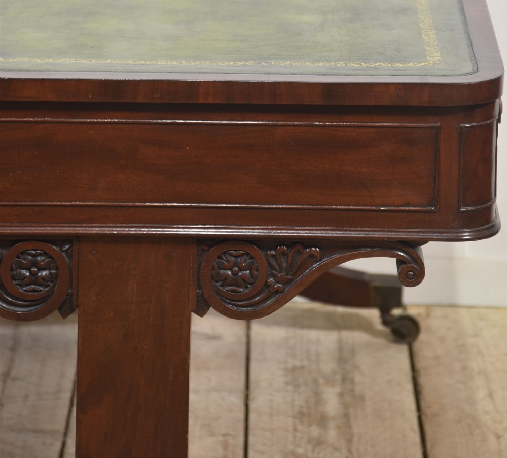 A Regency mahogany library table featuring a green leather inset top, brass knob drawers, a turned central stretcher, and reeded sabre legs on brass castors. View XV