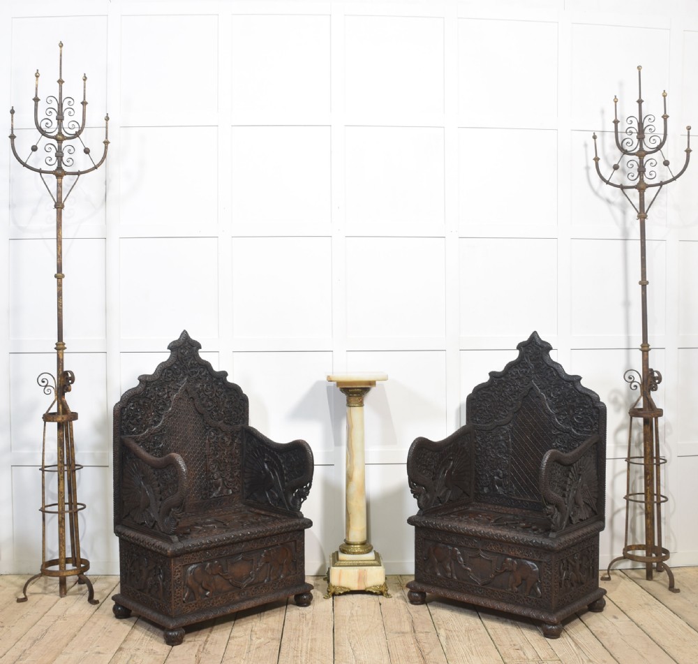 A pair of 19th-century dark hardwood ceremonial armchairs featuring intricate relief carvings, arched backrests, and elephant motifs on the base panels. View II