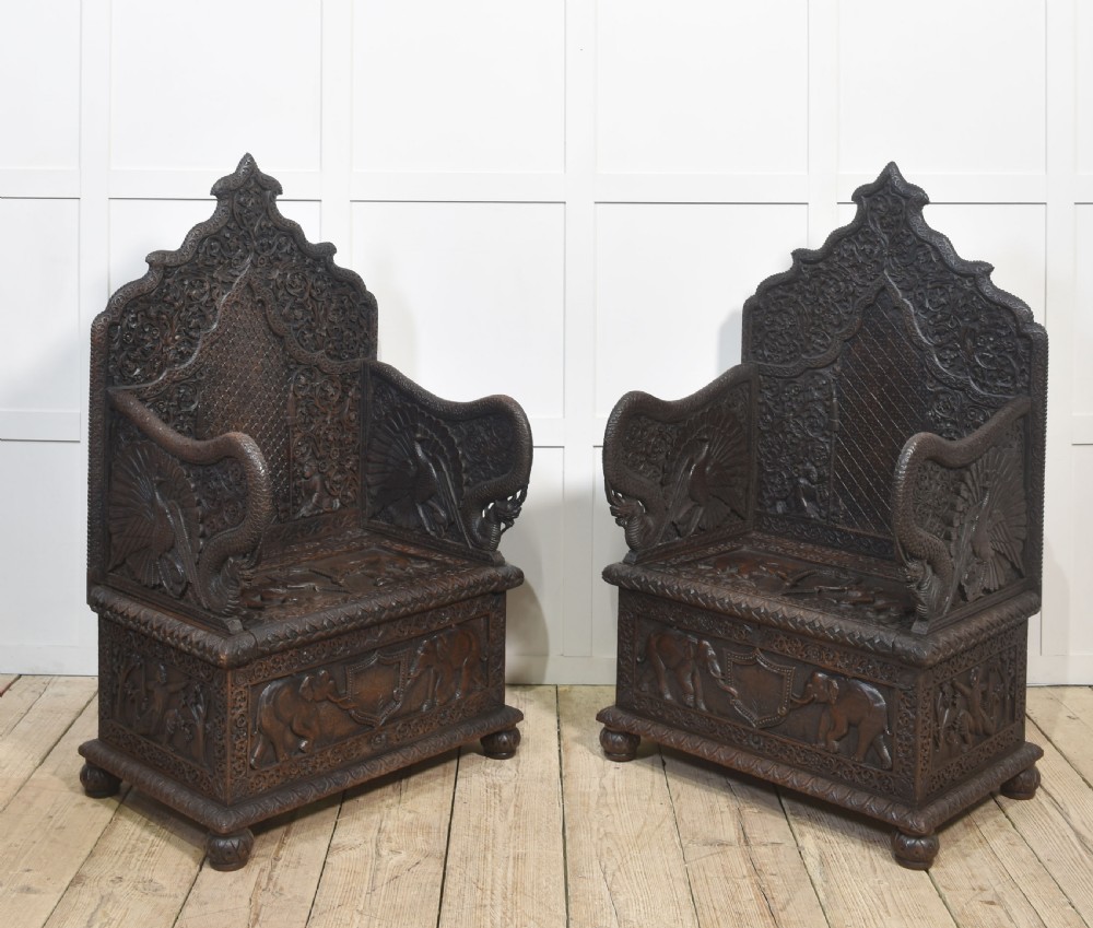 A pair of 19th-century dark hardwood ceremonial armchairs featuring intricate relief carvings, arched backrests, and elephant motifs on the base panels. View III