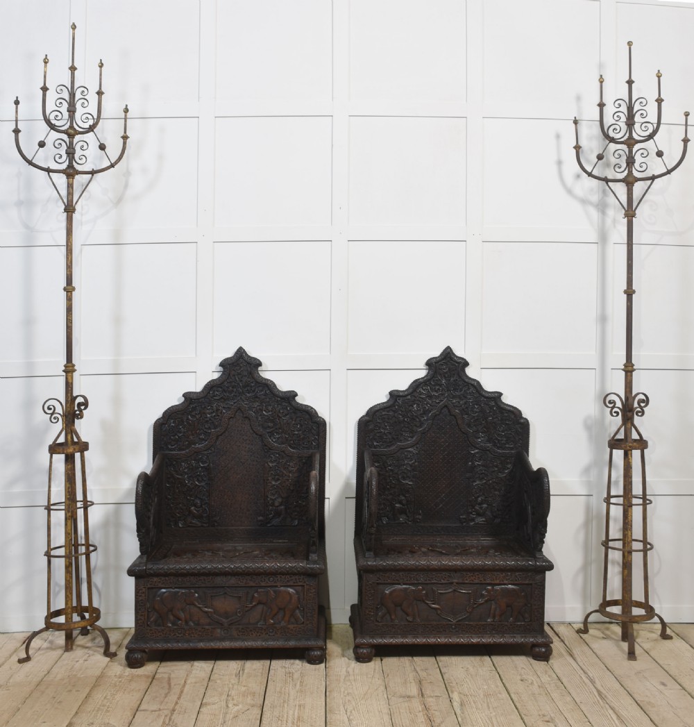 A pair of 19th-century dark hardwood ceremonial armchairs featuring intricate relief carvings, arched backrests, and elephant motifs on the base panels. View VII