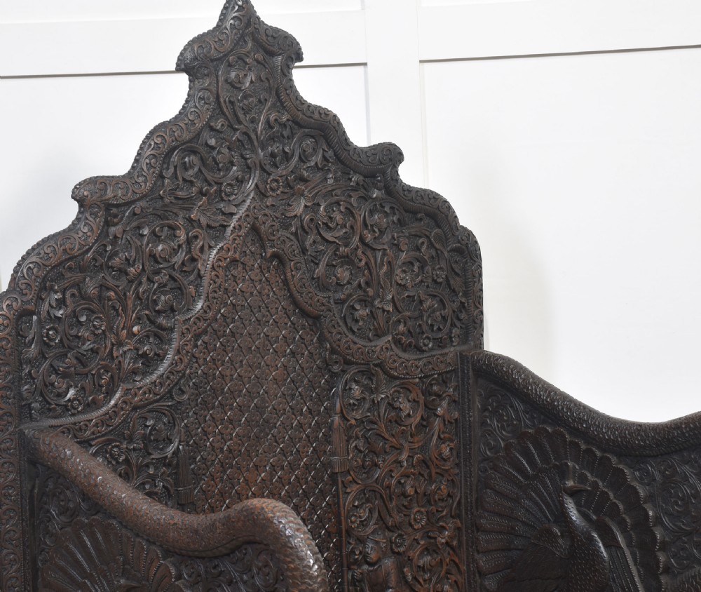 A pair of 19th-century dark hardwood ceremonial armchairs featuring intricate relief carvings, arched backrests, and elephant motifs on the base panels. View IX