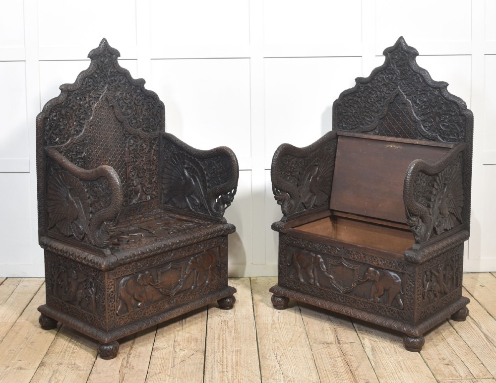 A pair of 19th-century dark hardwood ceremonial armchairs featuring intricate relief carvings, arched backrests, and elephant motifs on the base panels. View XII