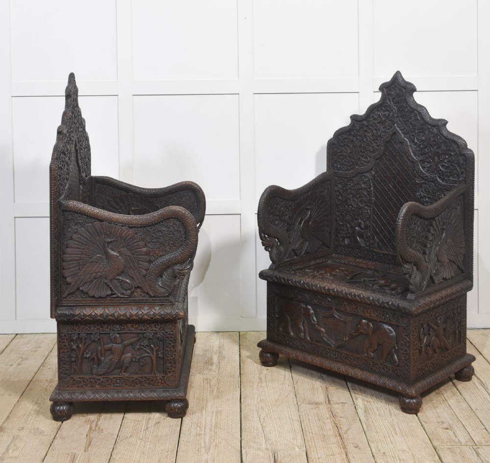A pair of 19th-century dark hardwood ceremonial armchairs featuring intricate relief carvings, arched backrests, and elephant motifs on the base panels. View XIII