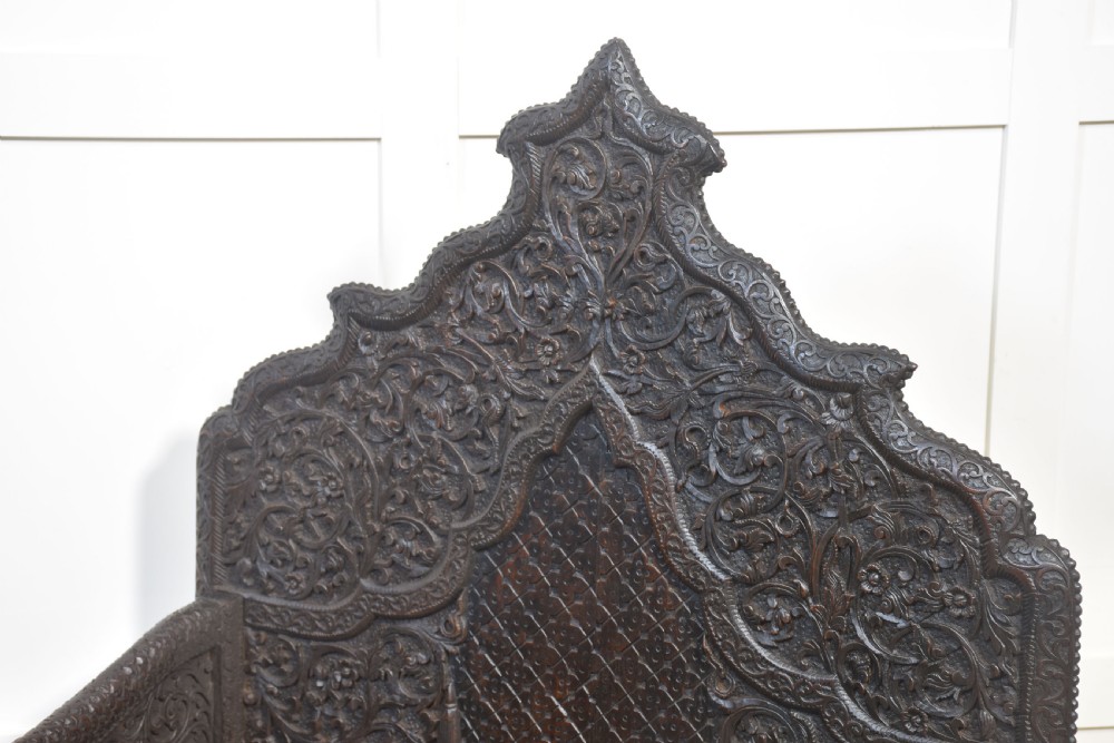 A pair of 19th-century dark hardwood ceremonial armchairs featuring intricate relief carvings, arched backrests, and elephant motifs on the base panels. View XV