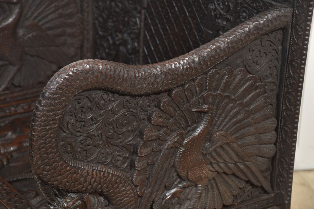 A pair of 19th-century dark hardwood ceremonial armchairs featuring intricate relief carvings, arched backrests, and elephant motifs on the base panels. View XVI
