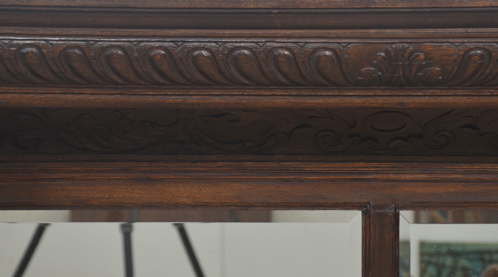A carved dark oak fire surround featuring twin mirror panels set above a wide hearth opening, framed by fluted columns and detailed leaf carvings. View VII