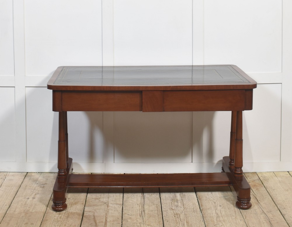 A mahogany writing table with a green leather inset top, two frieze drawers, turned trestle legs, and a stretcher base.