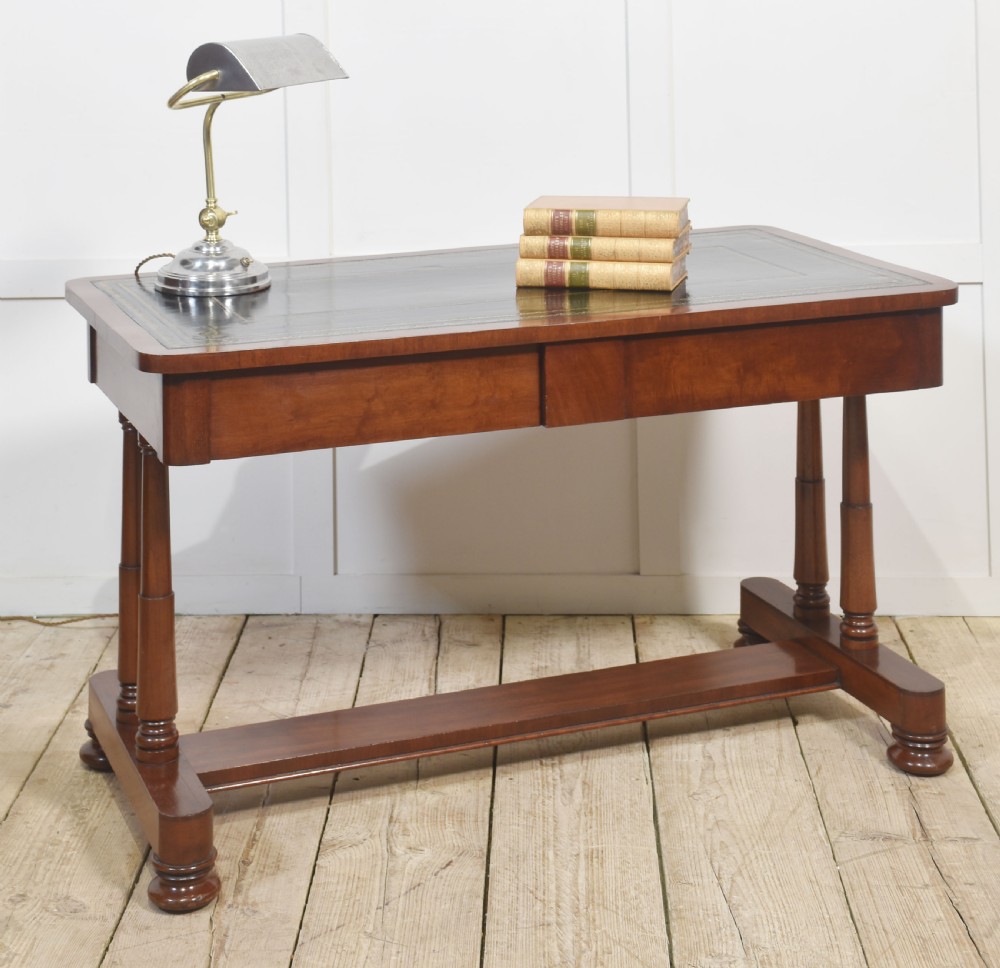 A mahogany writing table with a green leather inset top, two frieze drawers, turned trestle legs, and a stretcher base. View VI