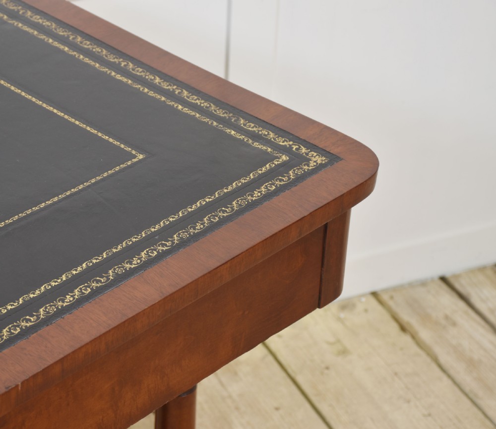 A mahogany writing table with a green leather inset top, two frieze drawers, turned trestle legs, and a stretcher base. View VII