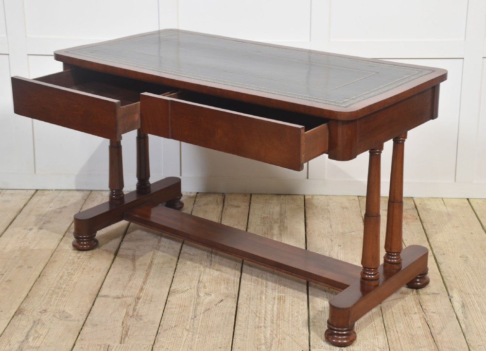 A mahogany writing table with a green leather inset top, two frieze drawers, turned trestle legs, and a stretcher base. View XII