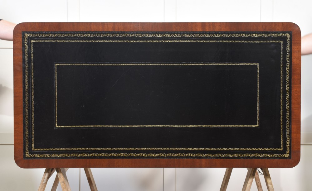 A mahogany writing table with a green leather inset top, two frieze drawers, turned trestle legs, and a stretcher base. View XIV