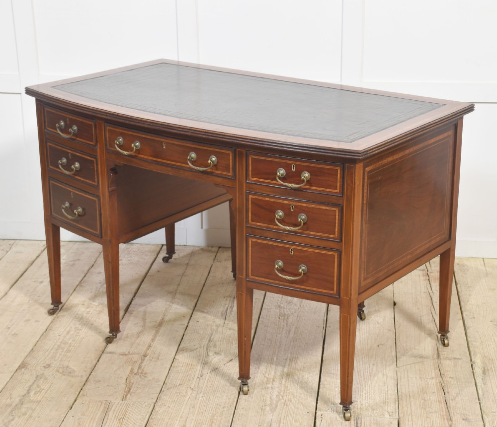 An antique mahogany writing desk featuring a leather insert top, boxwood stringing inlay, seven drawers with brass handles, and tapered legs on castors. View III
