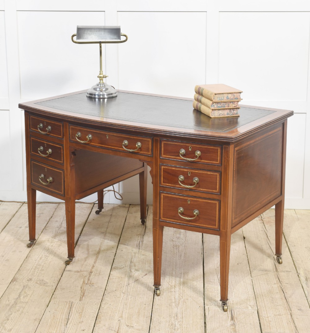 An antique mahogany writing desk featuring a leather insert top, boxwood stringing inlay, seven drawers with brass handles, and tapered legs on castors. View V