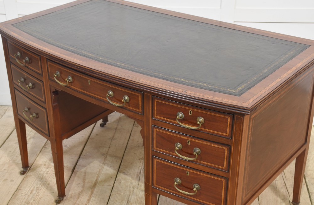 An antique mahogany writing desk featuring a leather insert top, boxwood stringing inlay, seven drawers with brass handles, and tapered legs on castors. View VIII