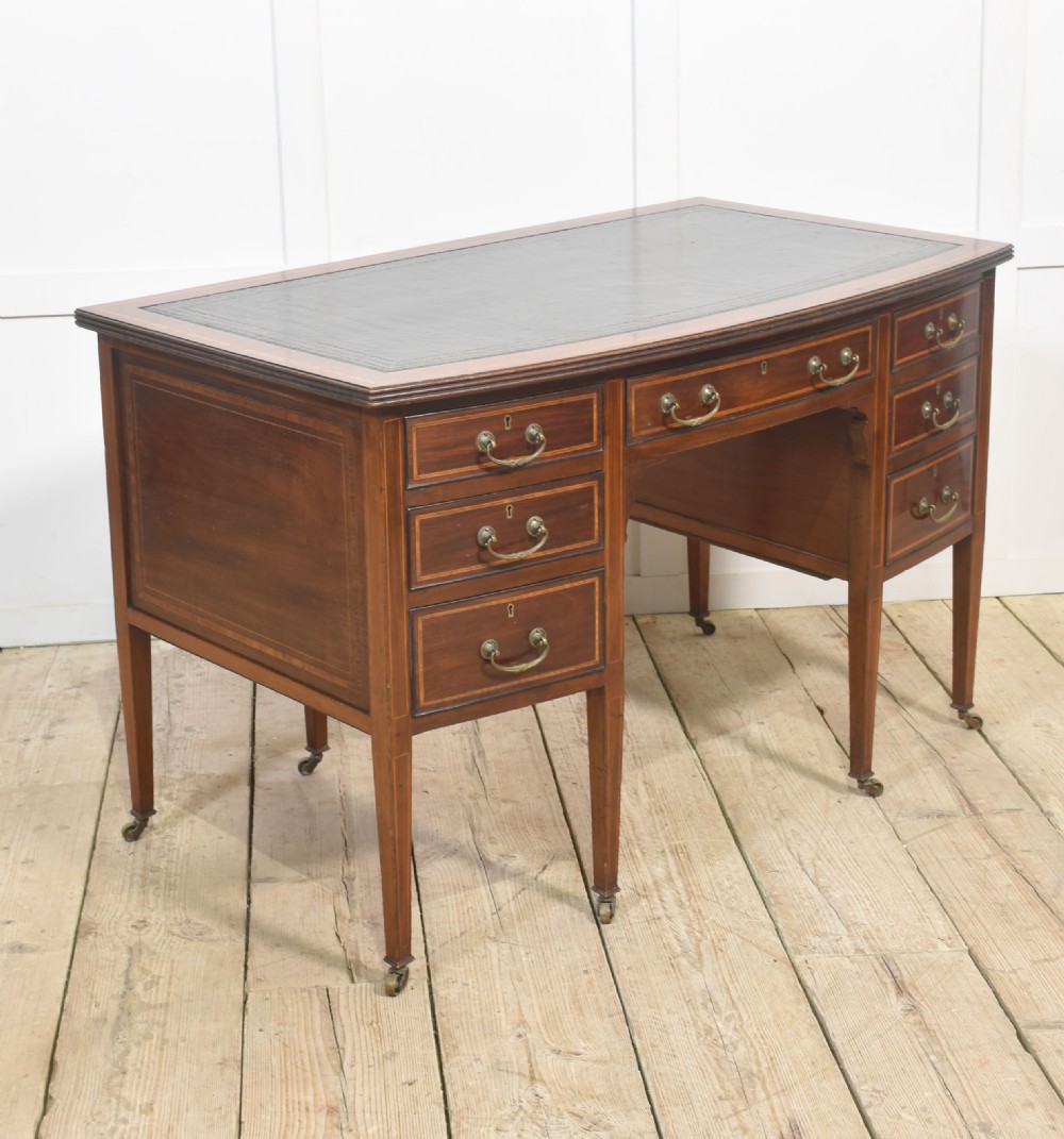 An antique mahogany writing desk featuring a leather insert top, boxwood stringing inlay, seven drawers with brass handles, and tapered legs on castors. View X
