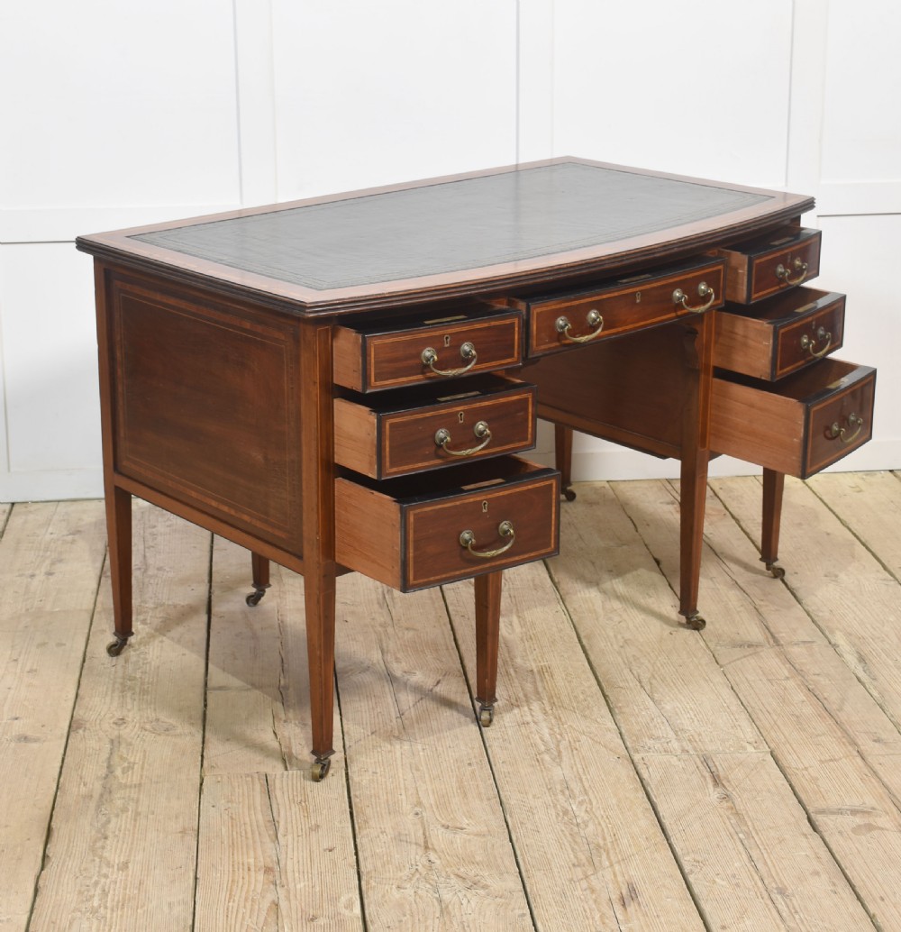 An antique mahogany writing desk featuring a leather insert top, boxwood stringing inlay, seven drawers with brass handles, and tapered legs on castors. View XII