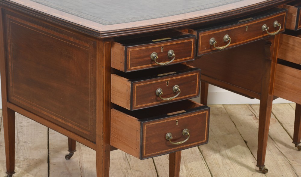 An antique mahogany writing desk featuring a leather insert top, boxwood stringing inlay, seven drawers with brass handles, and tapered legs on castors. View XIII