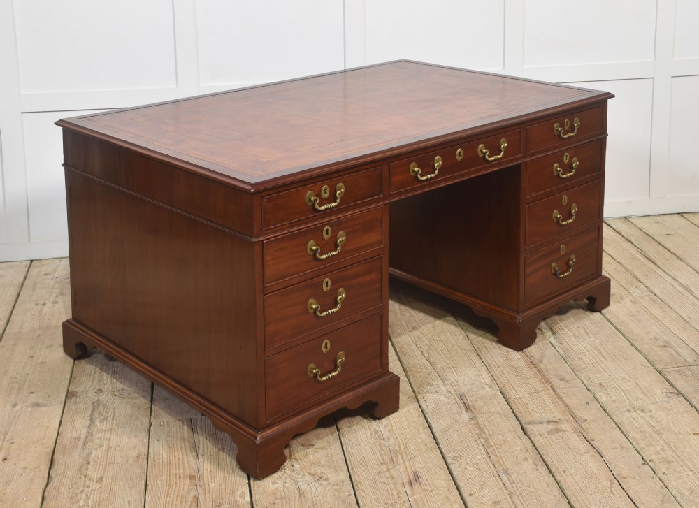 An antique mahogany partners desk featuring a leather-inset writing surface, brass swan-neck handles, twin pedestals, and ogee bracket feet.
