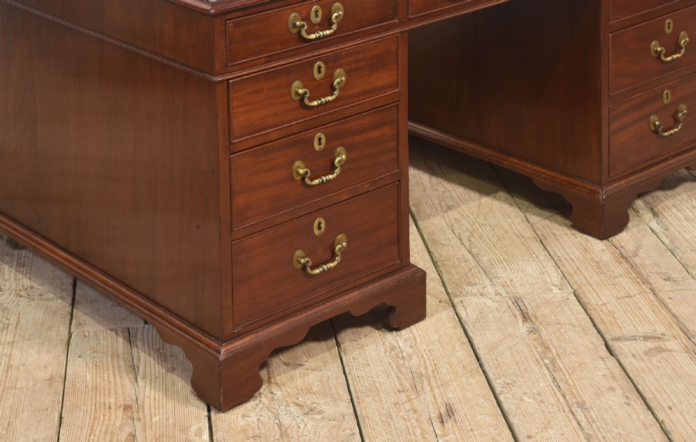An antique mahogany partners desk featuring a leather-inset writing surface, brass swan-neck handles, twin pedestals, and ogee bracket feet. View III