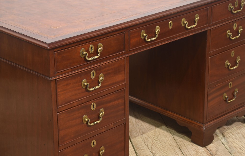 An antique mahogany partners desk featuring a leather-inset writing surface, brass swan-neck handles, twin pedestals, and ogee bracket feet. View V