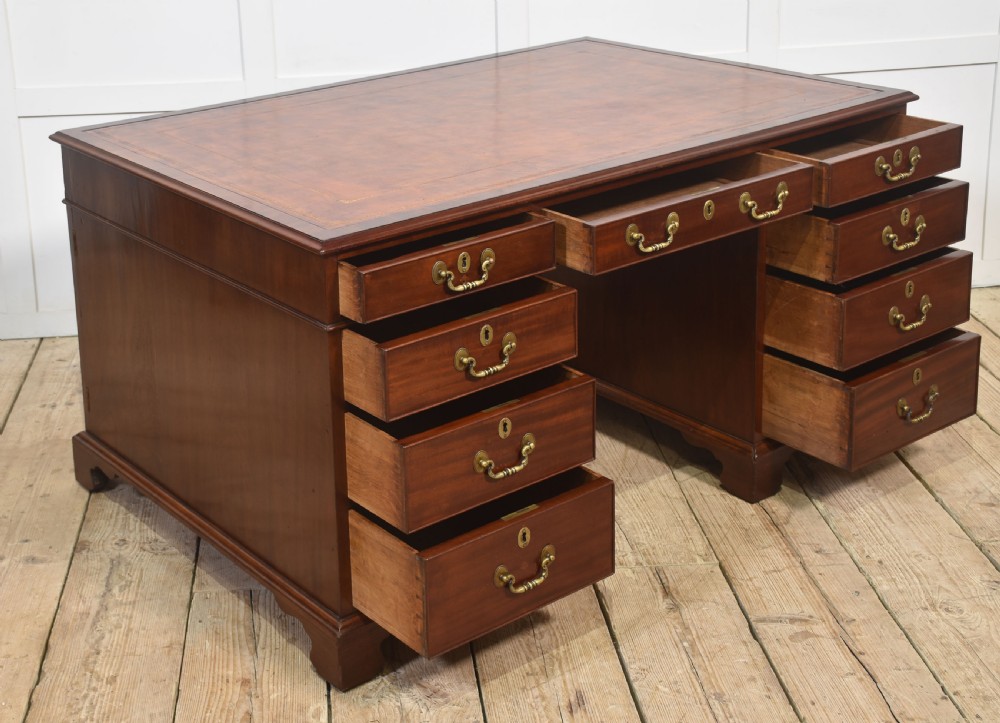 An antique mahogany partners desk featuring a leather-inset writing surface, brass swan-neck handles, twin pedestals, and ogee bracket feet. View VII