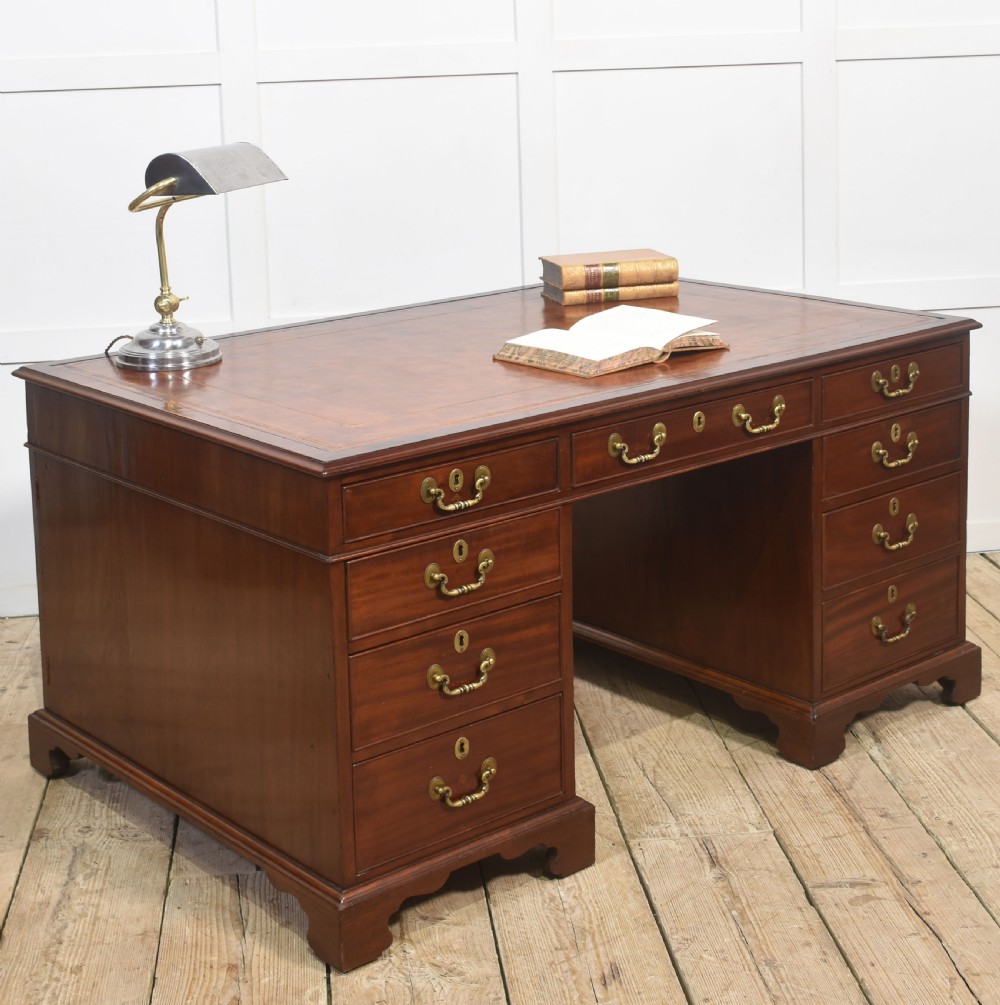 An antique mahogany partners desk featuring a leather-inset writing surface, brass swan-neck handles, twin pedestals, and ogee bracket feet. View VIII
