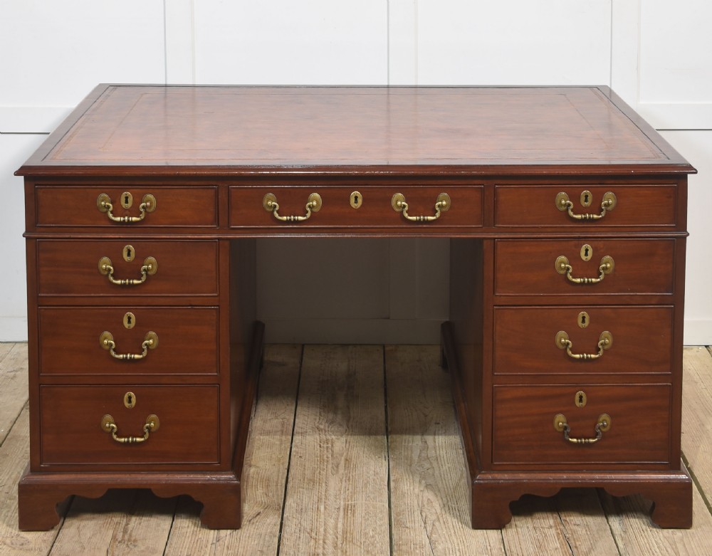 An antique mahogany partners desk featuring a leather-inset writing surface, brass swan-neck handles, twin pedestals, and ogee bracket feet. View IX