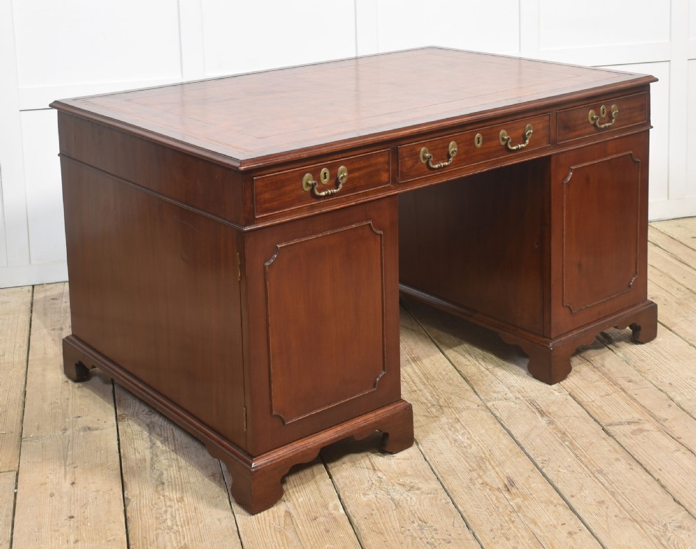An antique mahogany partners desk featuring a leather-inset writing surface, brass swan-neck handles, twin pedestals, and ogee bracket feet. View XII