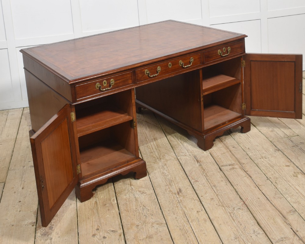 An antique mahogany partners desk featuring a leather-inset writing surface, brass swan-neck handles, twin pedestals, and ogee bracket feet. View XIII