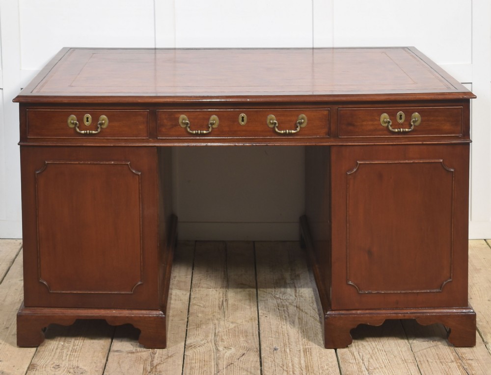An antique mahogany partners desk featuring a leather-inset writing surface, brass swan-neck handles, twin pedestals, and ogee bracket feet. View XIV