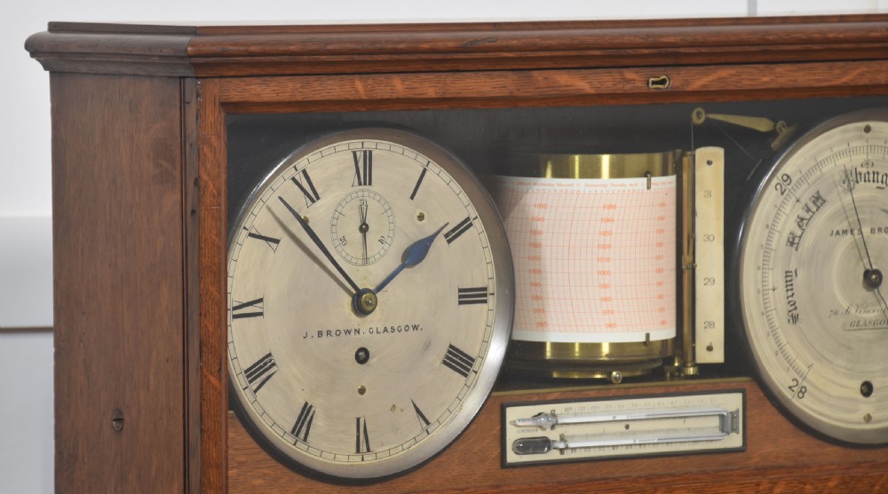 A glazed oak-cased antique weather station featuring a clock dial on the left, an aneroid barometer on the right, and a central paper drum barograph with an integrated thermometer. View III